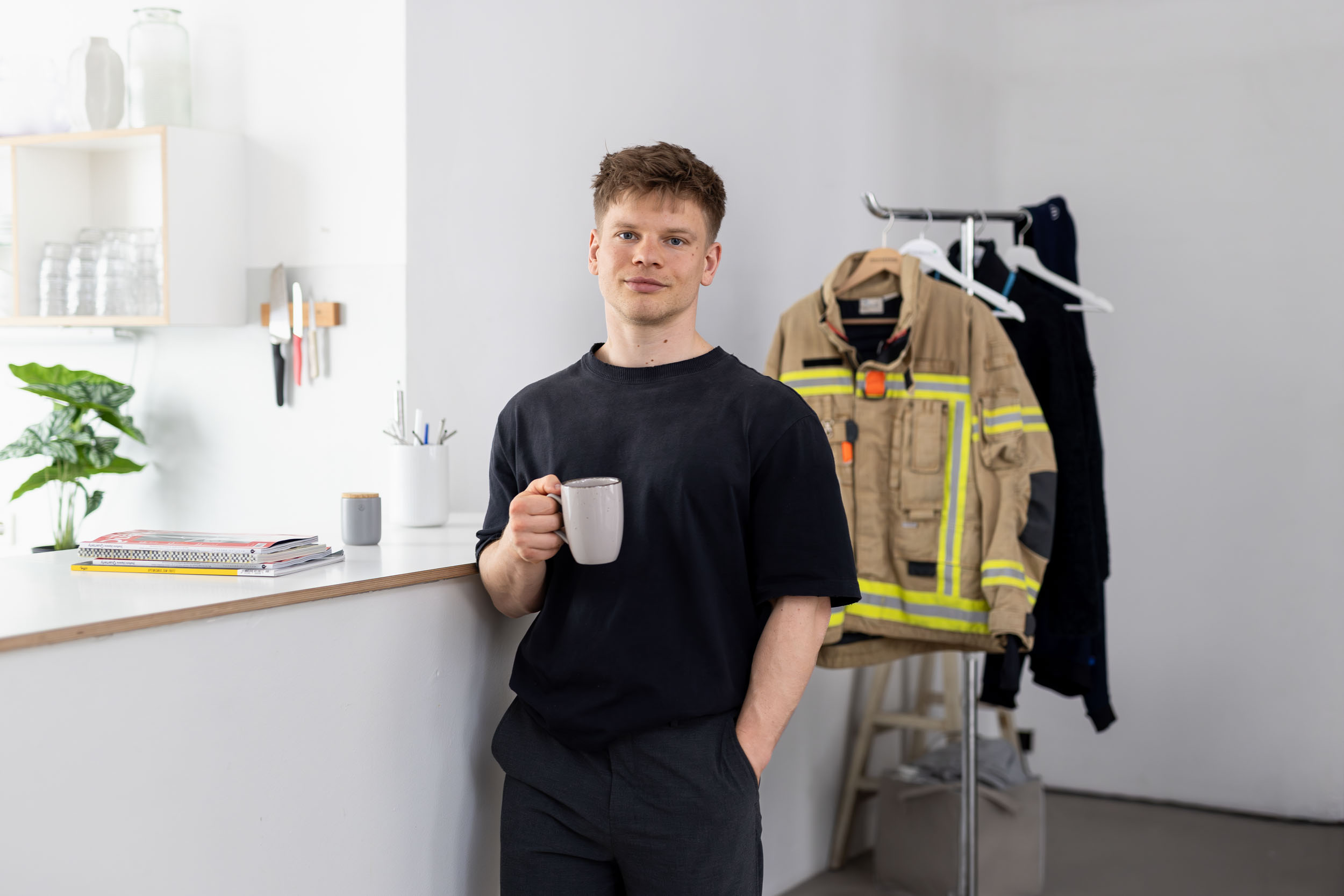 Ein bei der Landesfeuerwehr beschäftigter junger Mann lehnt mit einem Kaffeebecher an der Küchentheke seines Apartments.