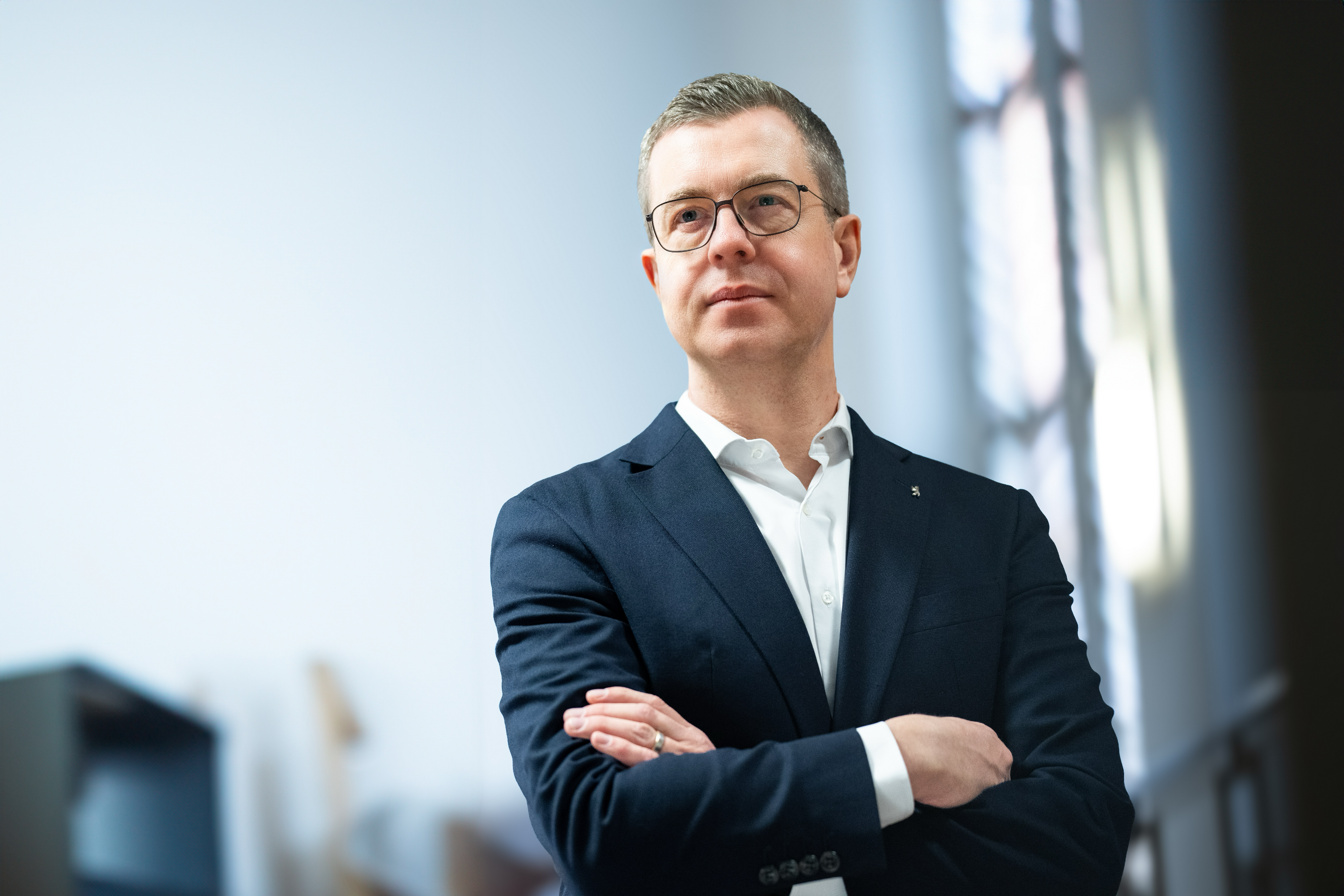 Der Berliner Finanzsenator Stefan Evers im eleganten Anzug vor einer blauen Fotowand.
