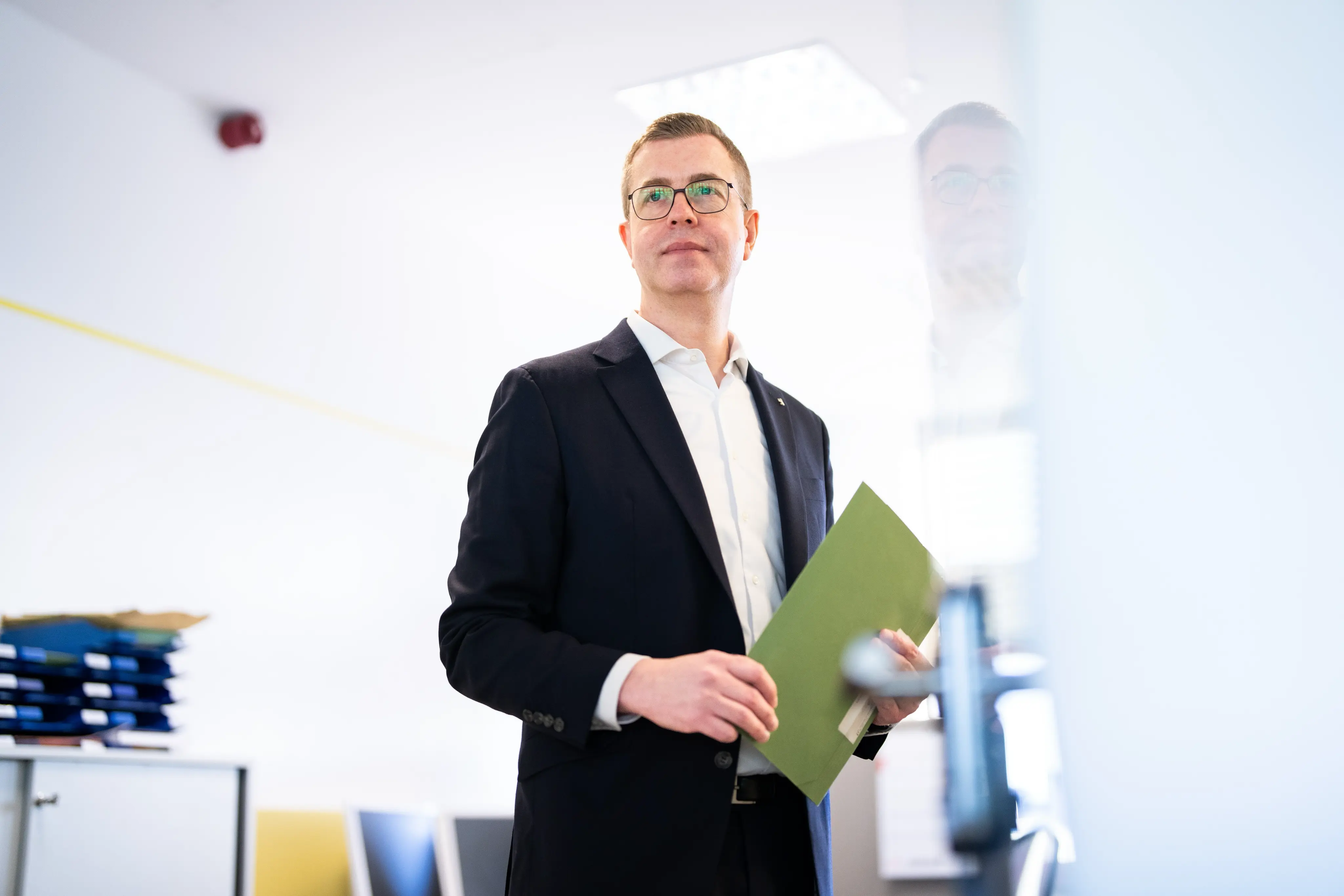 Der Berliner Finanzsenators Stefan Evers steht mit einer Mappe in der Hand in einem Büro.
